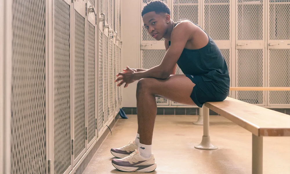 Młody mężczyzna w sportowym stroju siedzi na ławce w szatni, nosząc sneakersy New Balance FuelCell Rebel v5